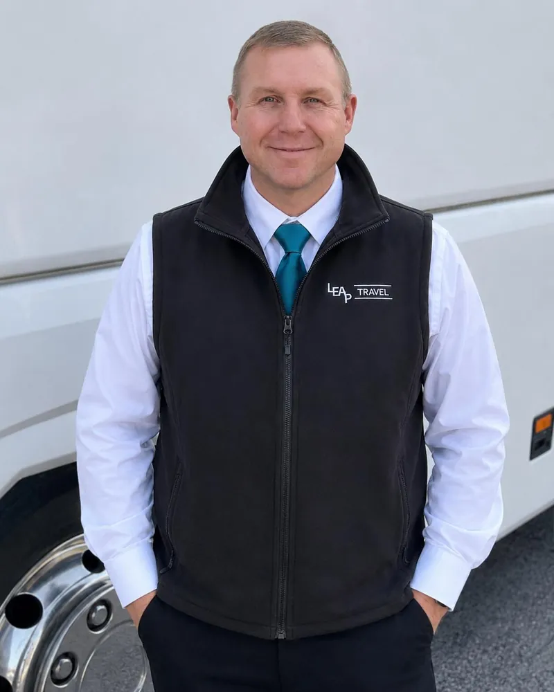 Jim, Leap Travel coach driver, in uniform beside a coach